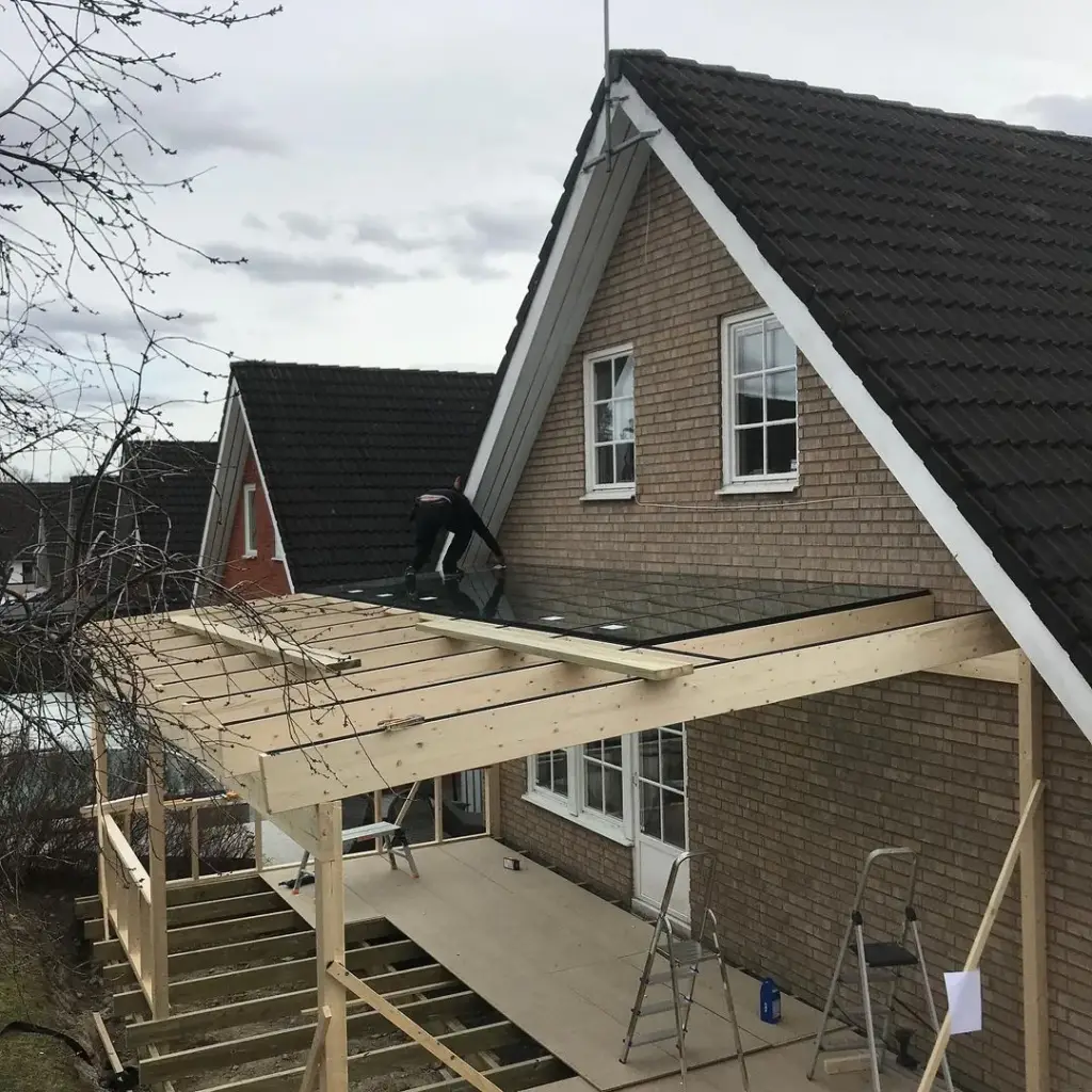 Altan under byggnation med pergola och glastak intill ett tegelhus